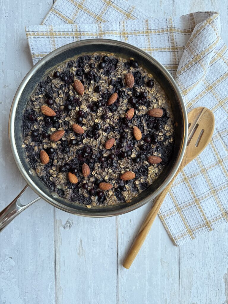Wild blueberry oatmeal skillet presented in frying pan beside a wood spoon.