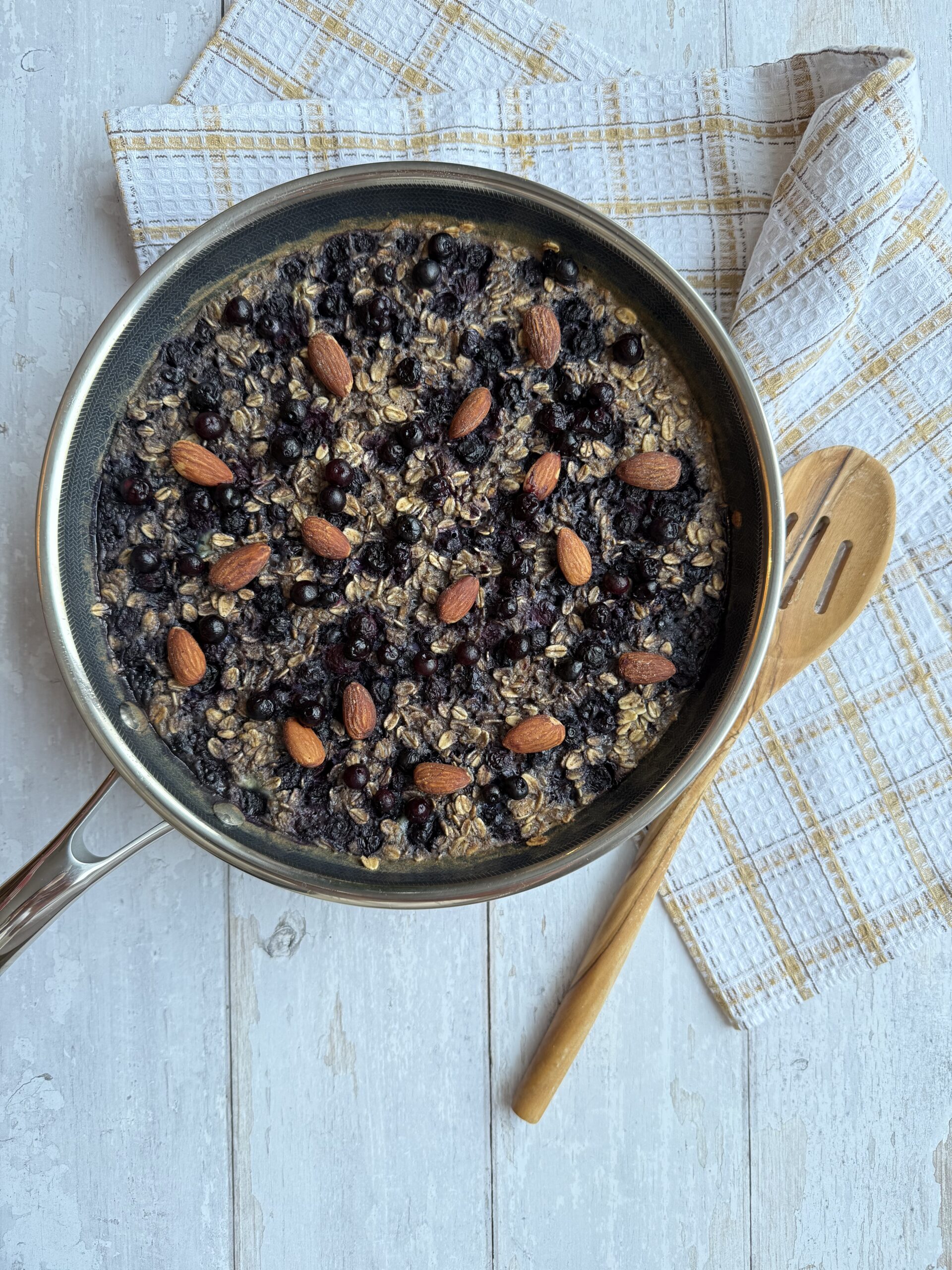 Wild blueberry oatmeal skillet presented in frying pan beside a wood spoon.