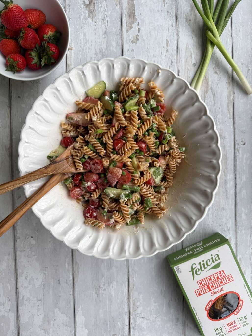Bowl of high fiber pasta salad on white table surrounded by strawberries and green onions